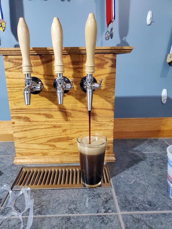 A brewer happily pouring from a kegerator, leaving a pile of empty bottles behind.